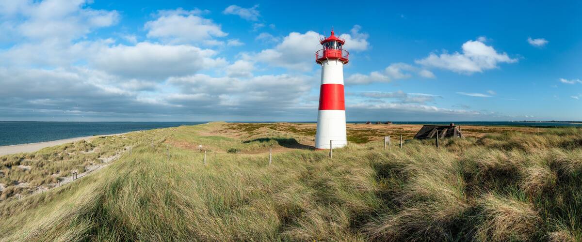 A red and white lighthouse on a grassy dune overlooking a beach.