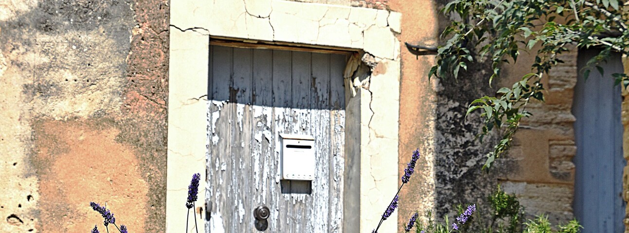 Un muro de piedra rústico, una puerta de madera desgastada y plantas de lavanda en un jardín.