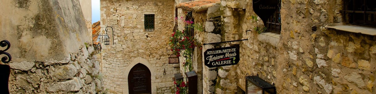 Une rue étroite bordée de bâtiments en pierre, une enseigne indiquant l’emplacement d’une galerie d’art et un clocher.