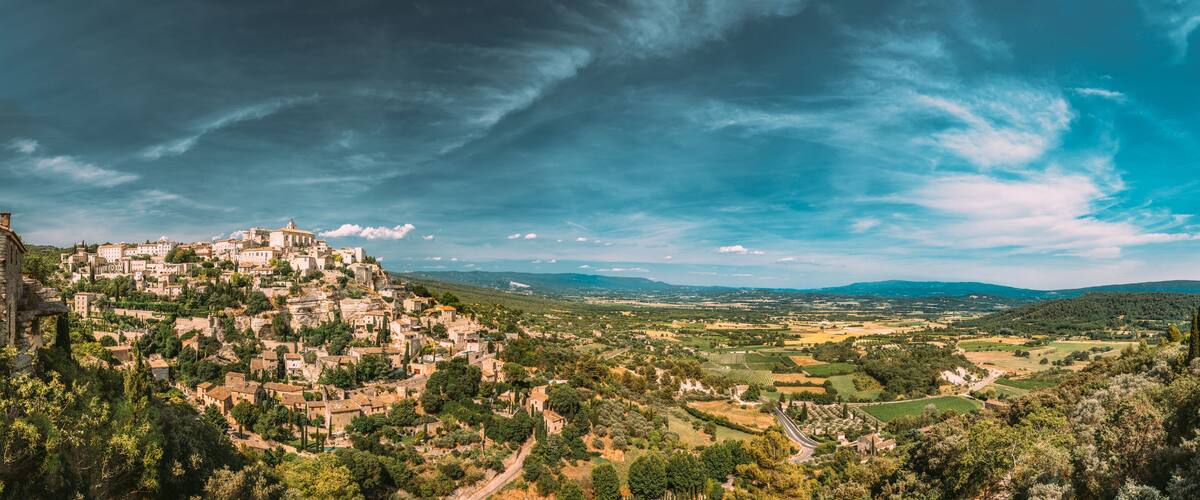 A mountainous town with historic buildings, terraced vineyards, and a clear sky.