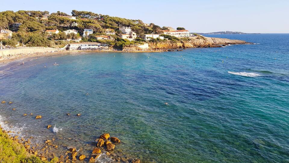 A coastal town with clear blue waters, rocky shoreline, and buildings on a hillside.