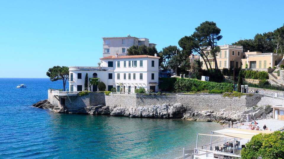 A coastal town with white buildings, a stone wall, and a clear blue sea.