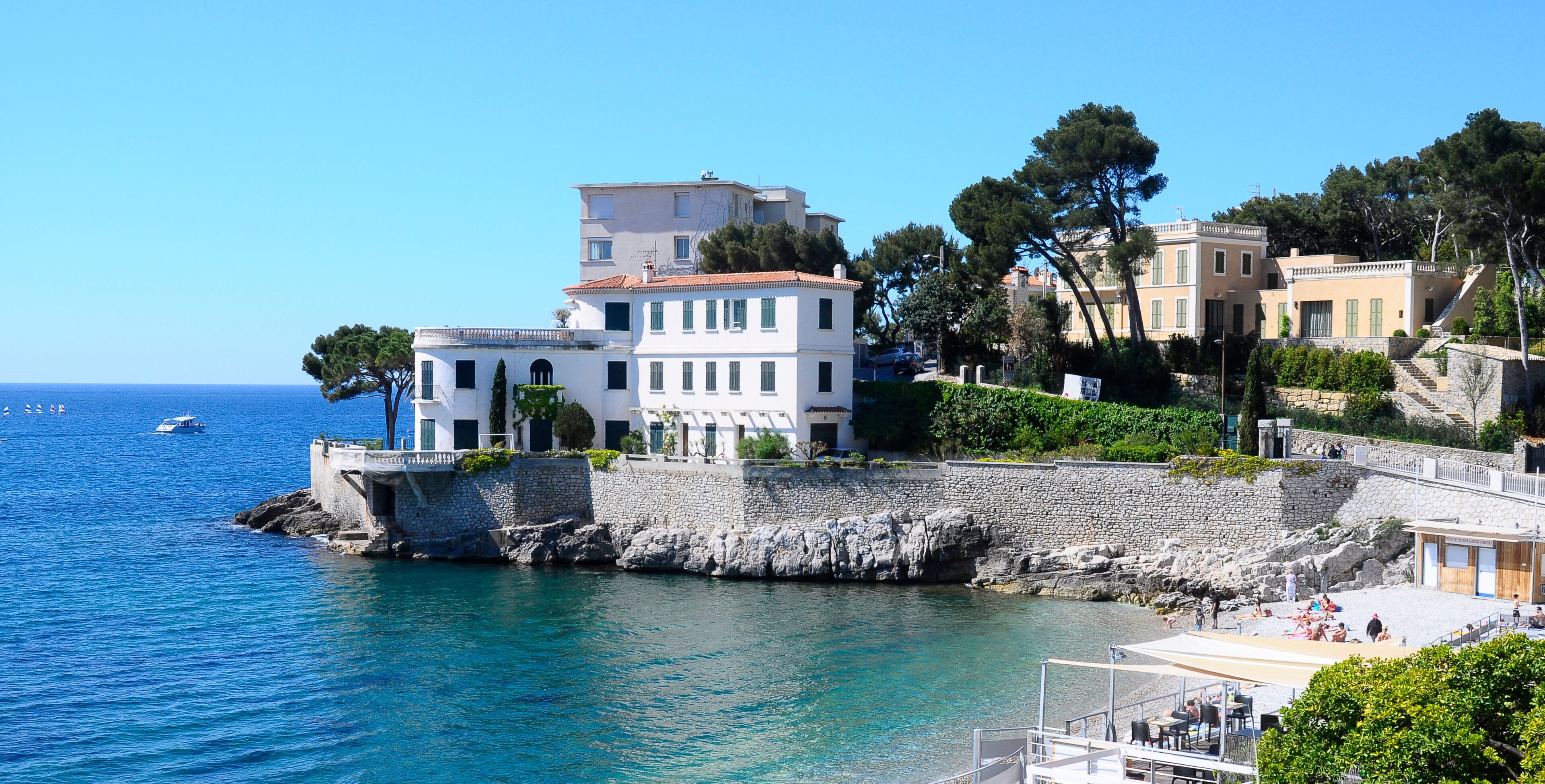 A coastal town with white buildings, a stone wall, and a clear blue sea.