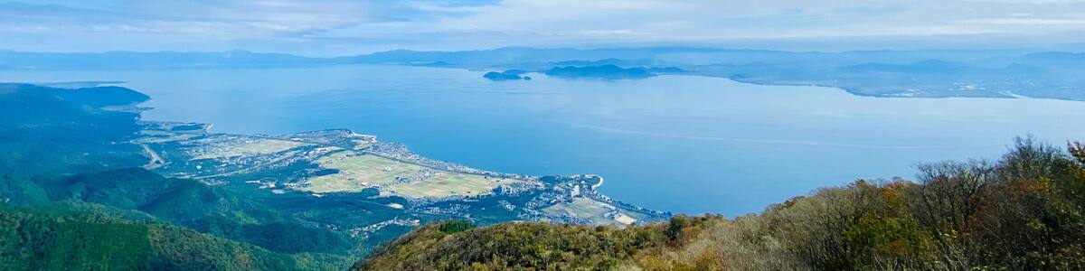 A coastal landscape with a clear sky, distant mountains, and a view of a town by the sea.