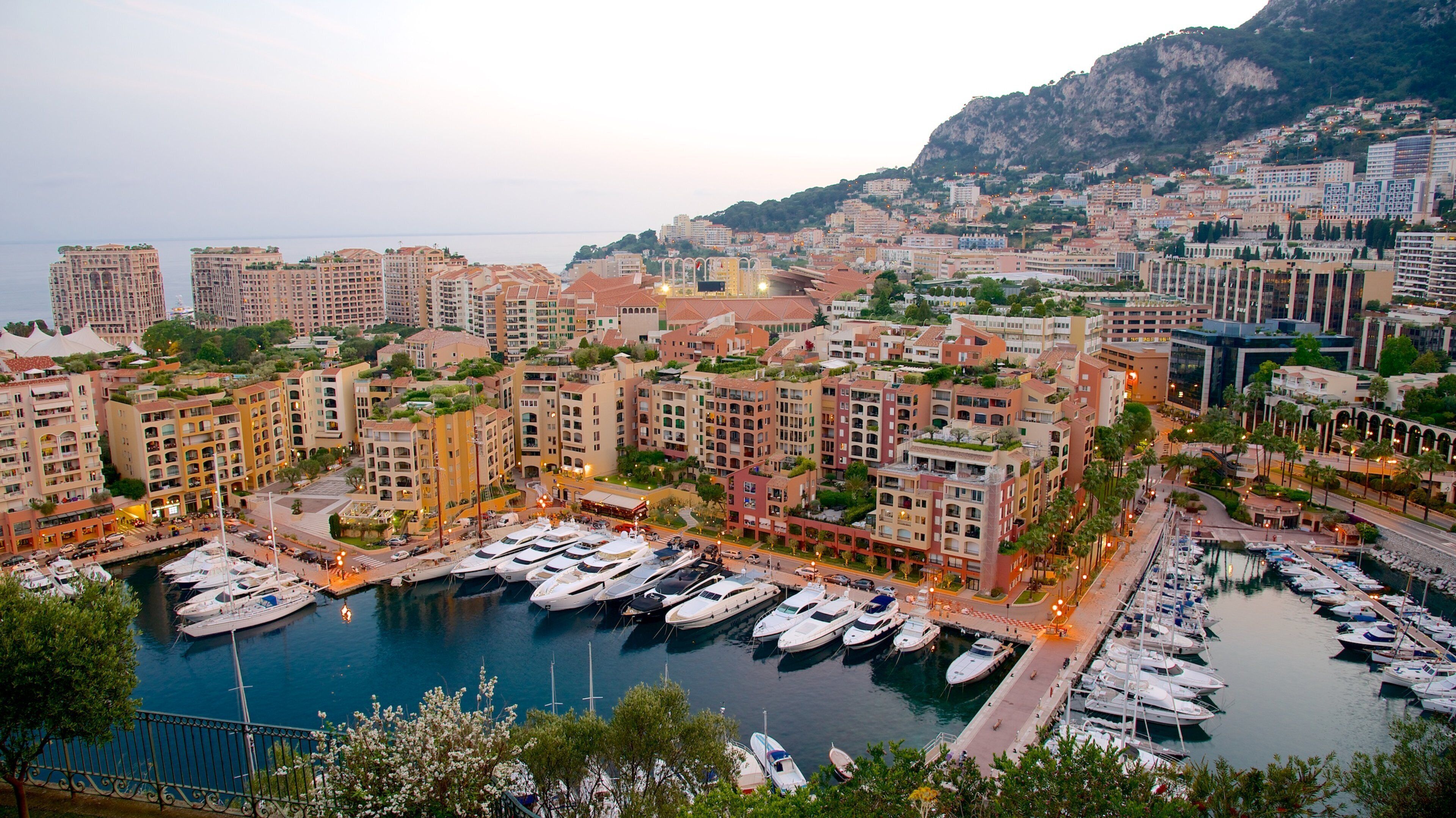 A marina with boats docked, surrounded by residential buildings and a mountainous backdrop.