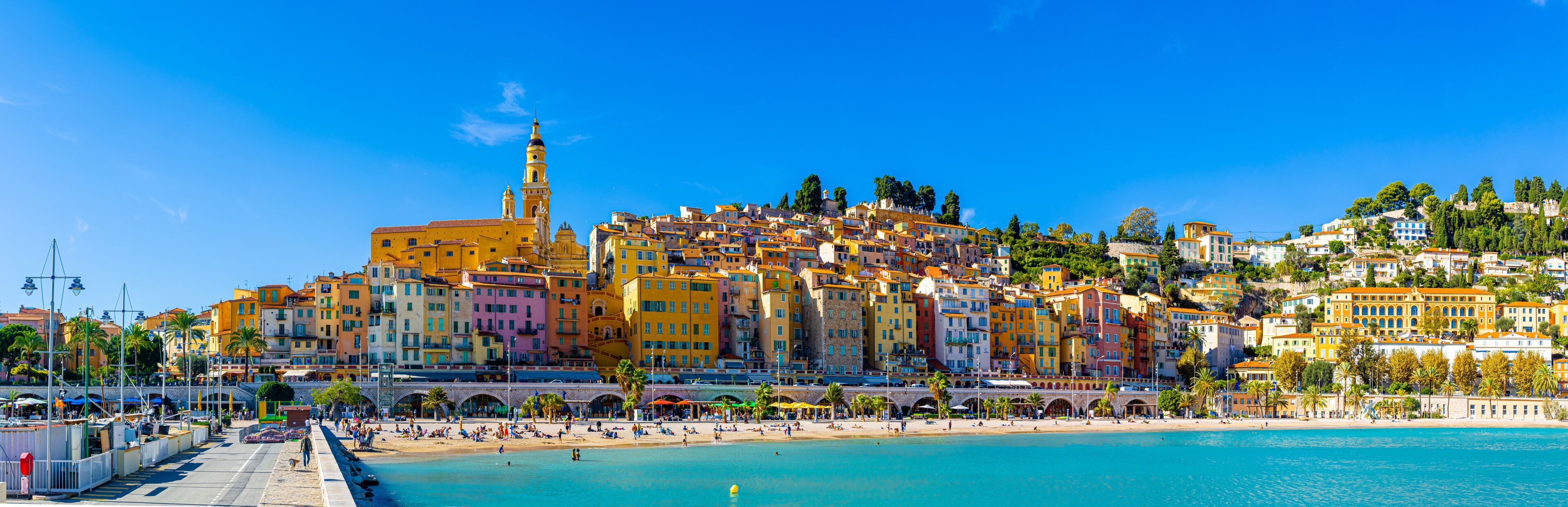 A coastal town with colorful buildings, a prominent church tower, and a beach.