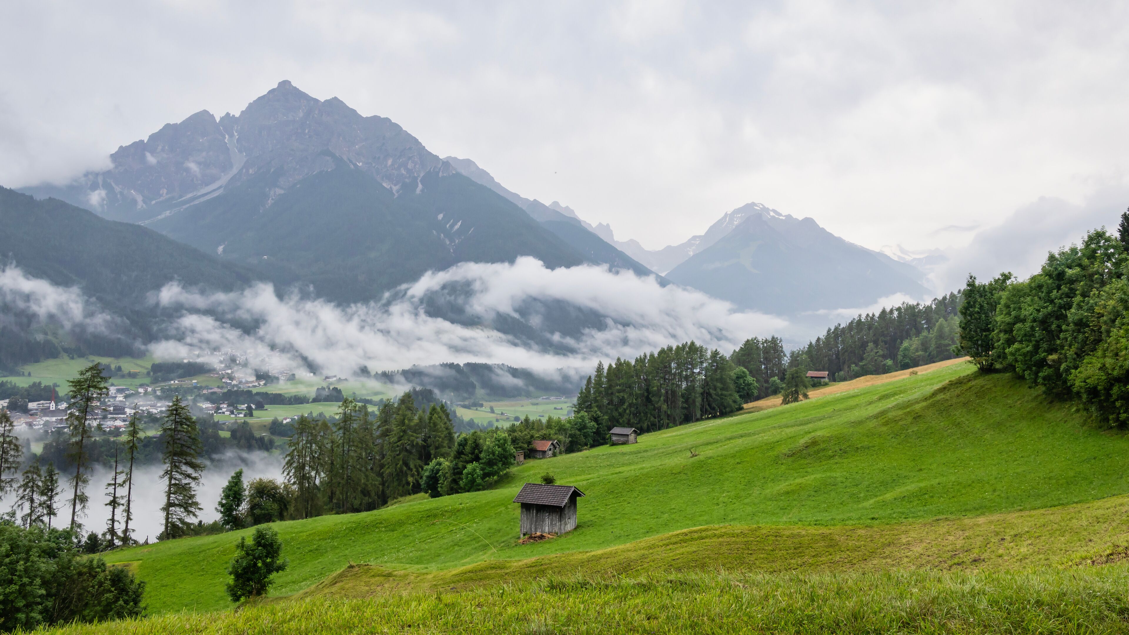 A green valley with a small wooden house, a church, and mountains in the background.
