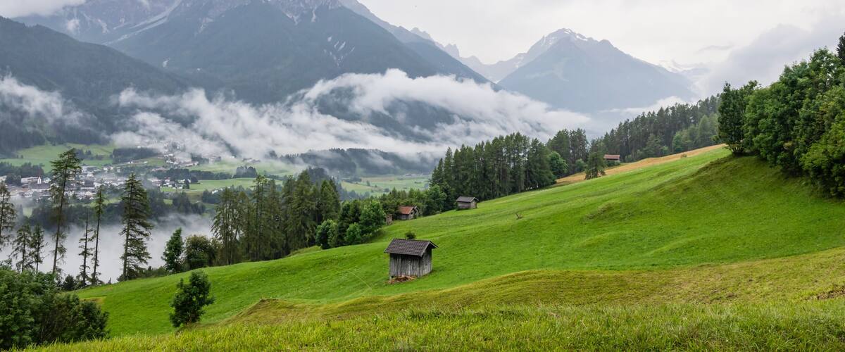 A green valley with a small wooden house, a church, and mountains in the background.