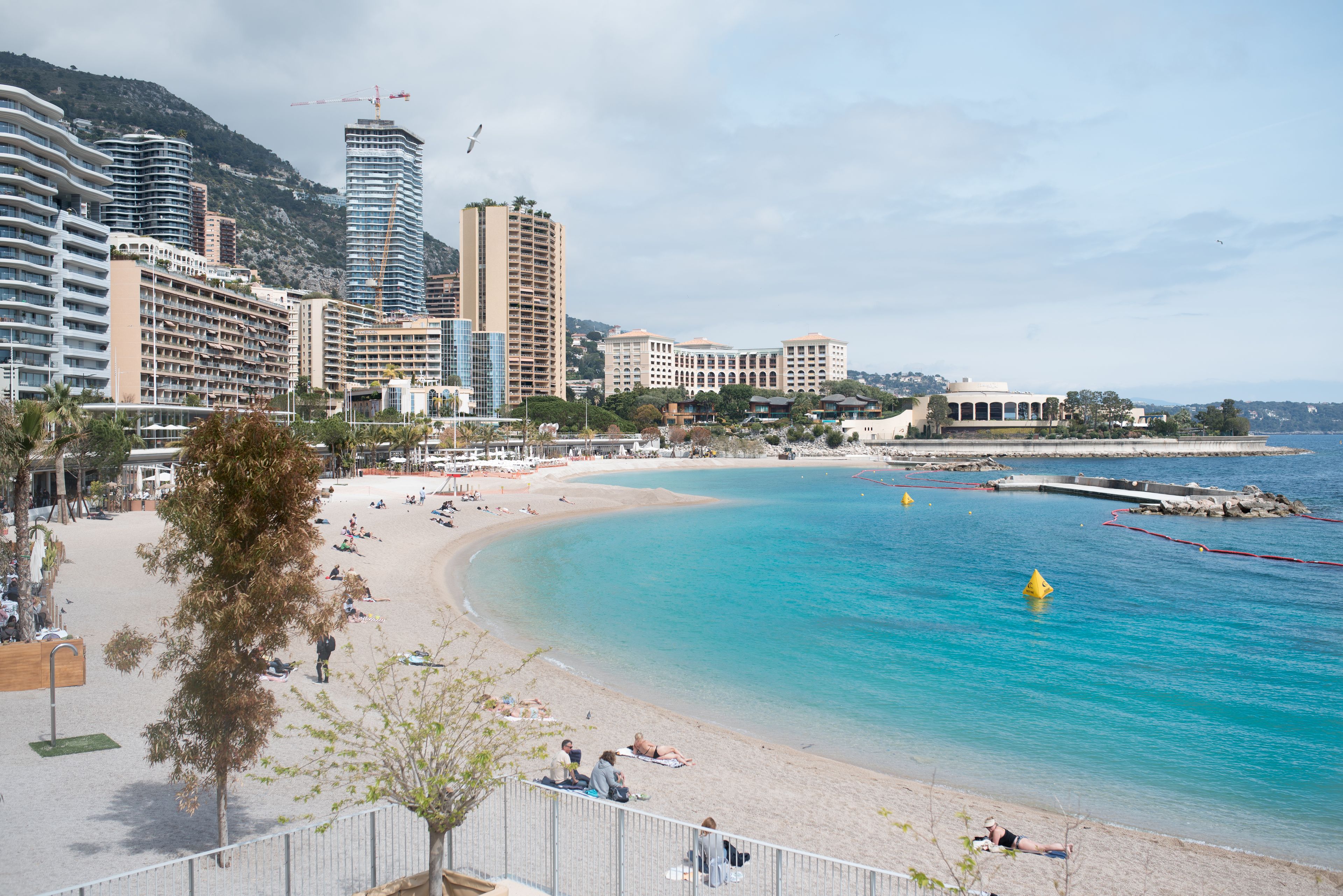 A coastal cityscape with a sandy beach, clear blue waters, and modern high-rise buildings.