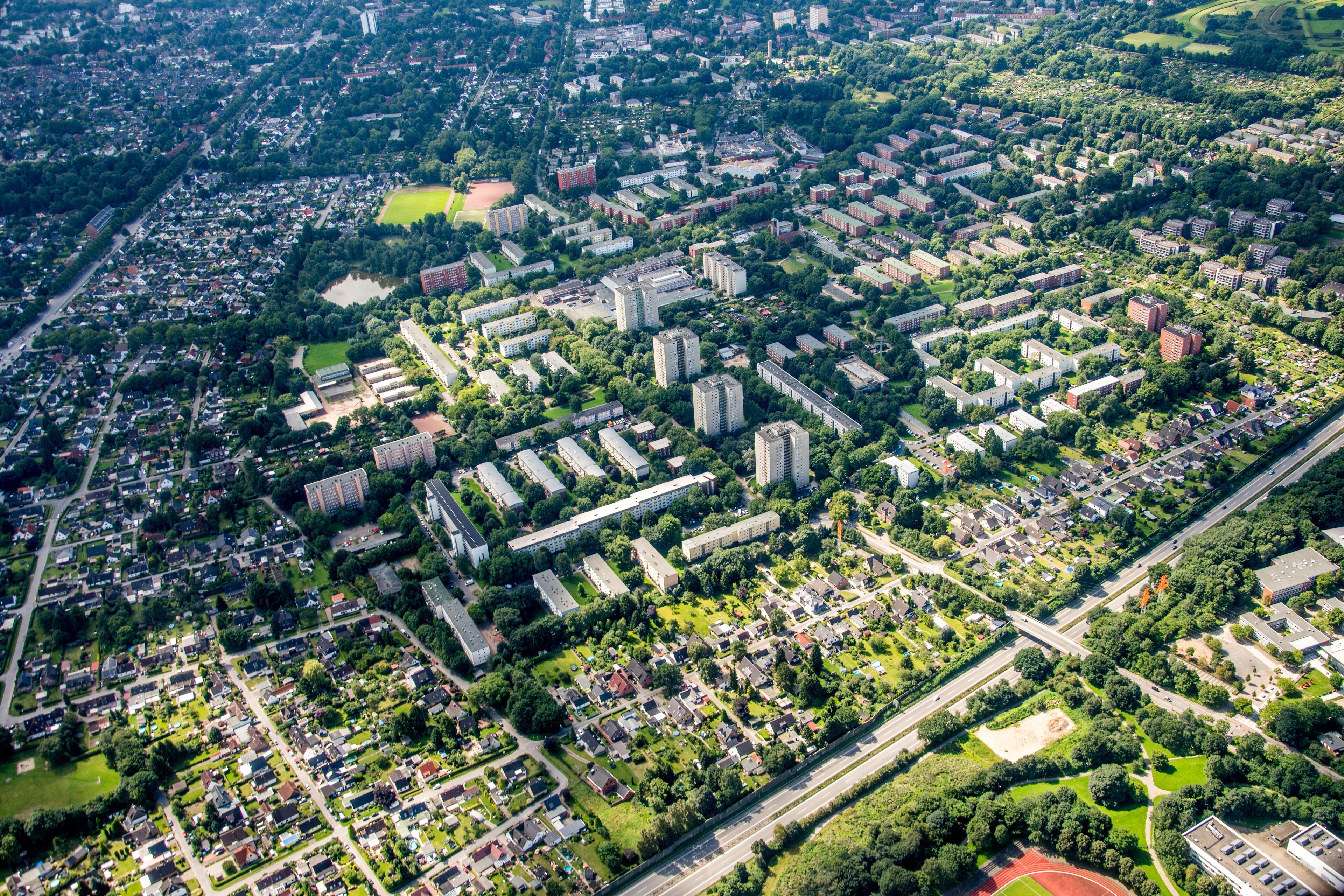 An aerial view of a densely populated urban area with residential buildings, green spaces, and a sports field.