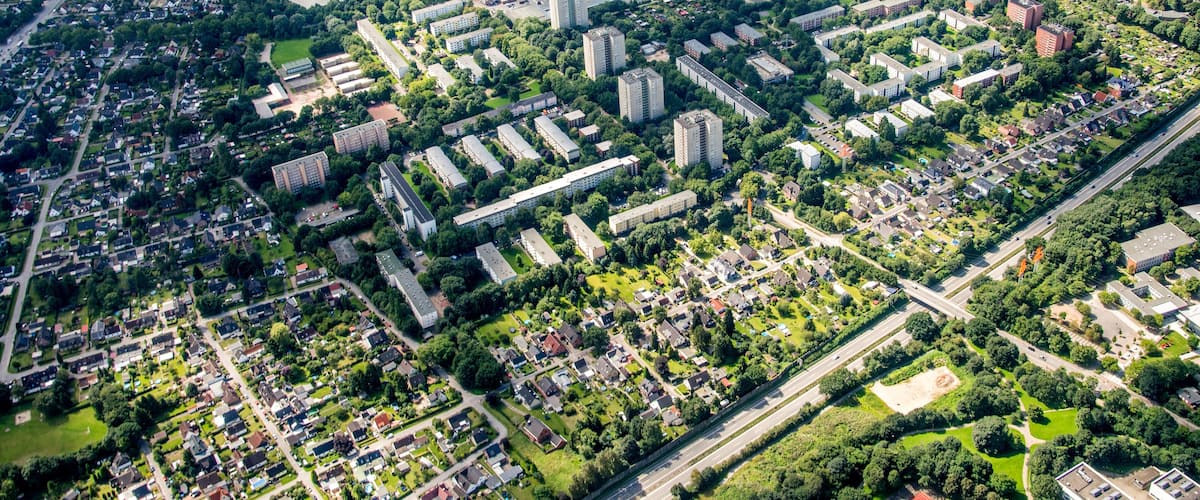 An aerial view of a densely populated urban area with residential buildings, green spaces, and a sports field.