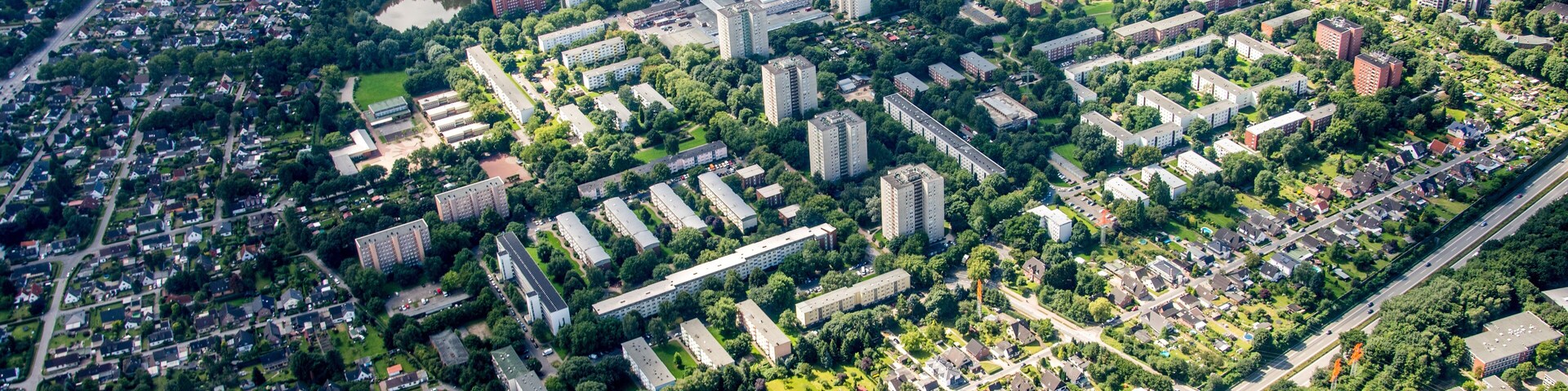 An aerial view of a densely populated urban area with residential buildings, green spaces, and a sports field.
