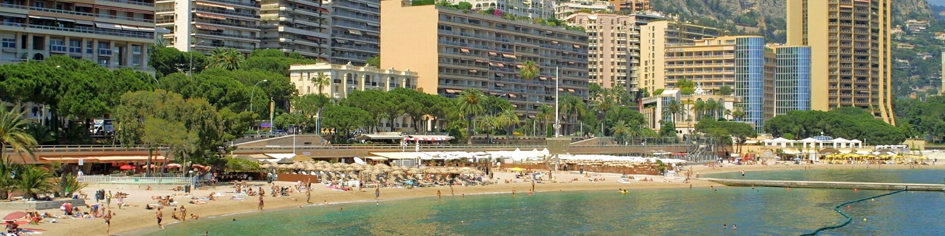 Un paysage urbain côtier avec une plage, de grands immeubles et une chaîne de montagnes en arrière-plan.