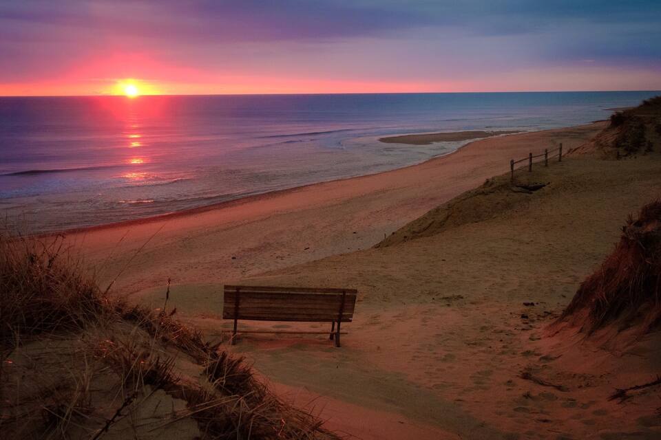 Una platja amb un banc de fusta, ones oceàniques i un capvespre.