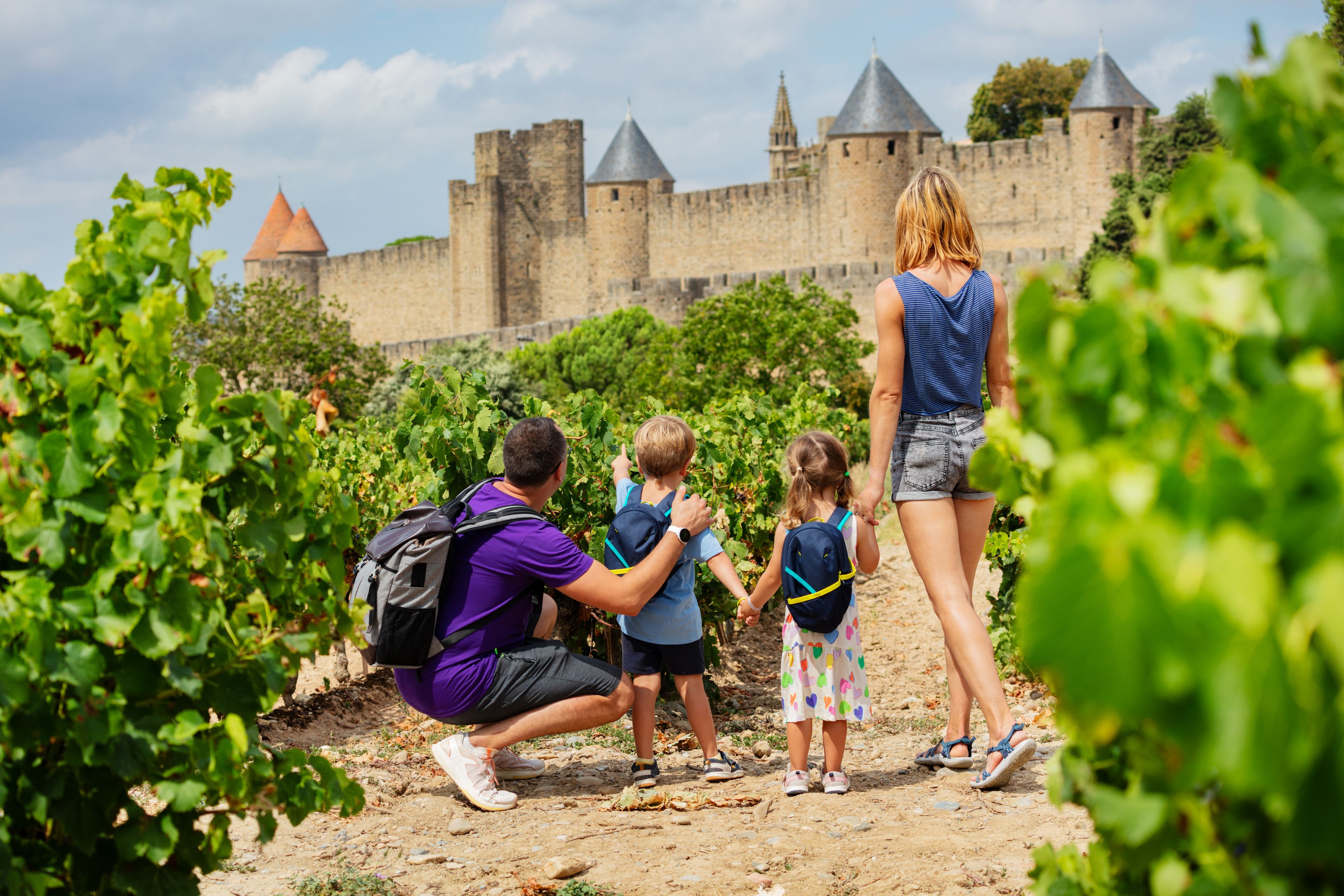 Uma família explora um vinhedo com um castelo histórico ao fundo.