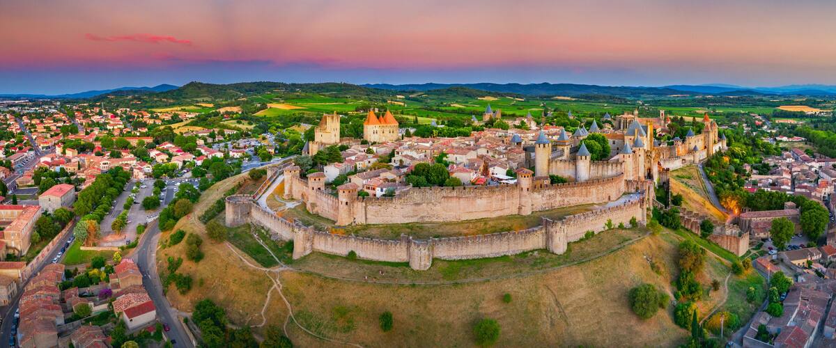 A medieval castle surrounded by a walled town with rolling hills in the background.
