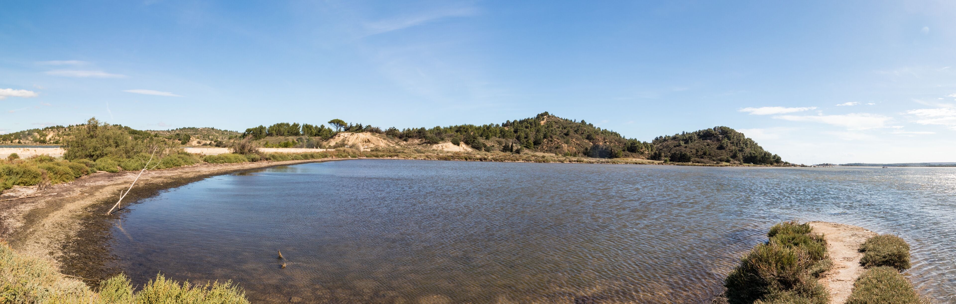 Un lago tranquilo de aguas cristalinas, rodeado de colinas y vegetación escasa.