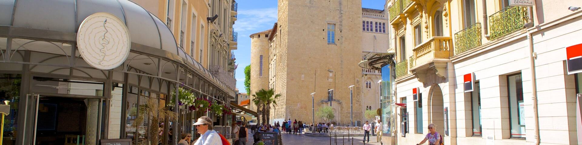 A cobblestone street lined with historic buildings, a prominent tower, and outdoor seating areas.