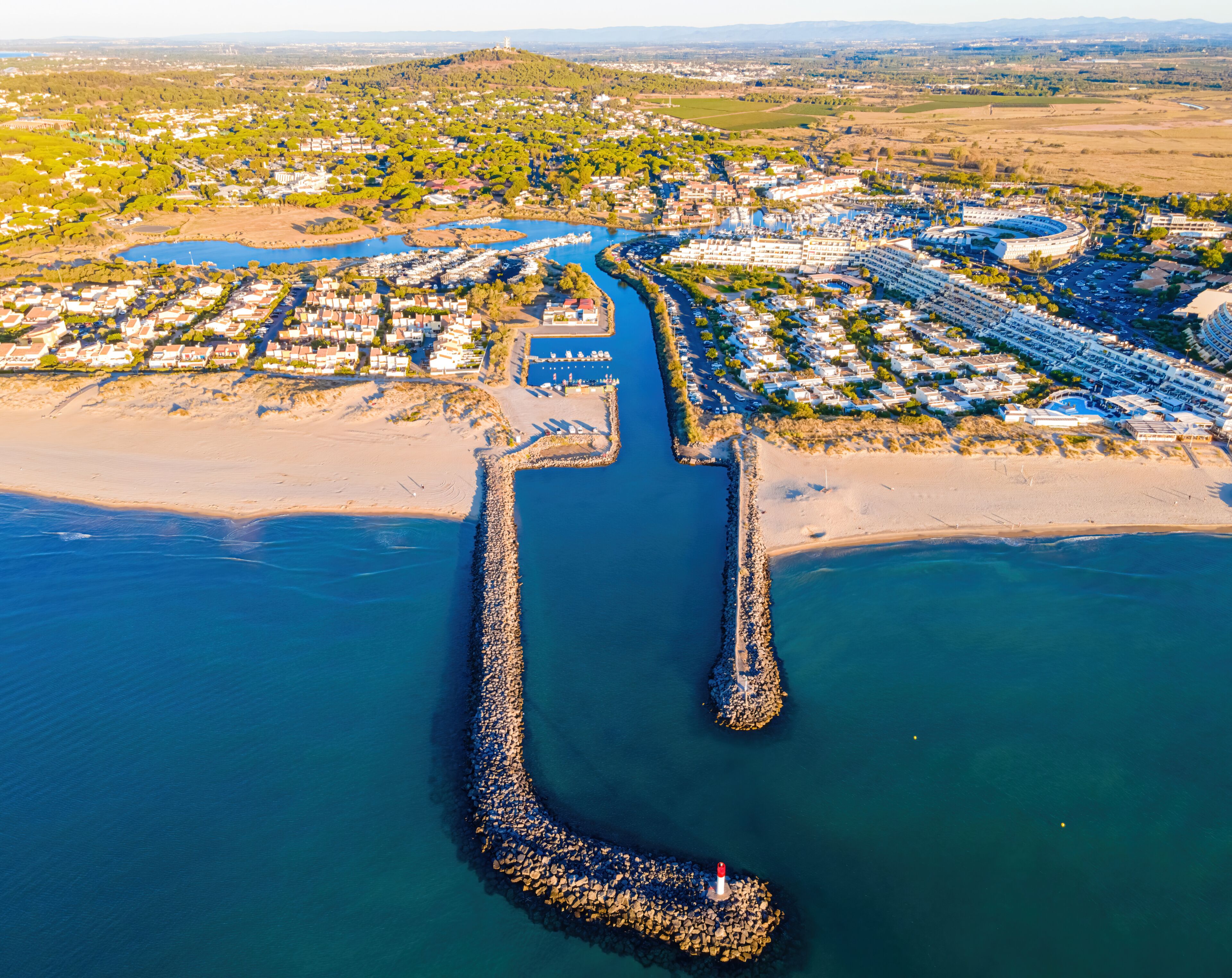 A coastal town with a marina, a lighthouse, and a river leading to the sea.