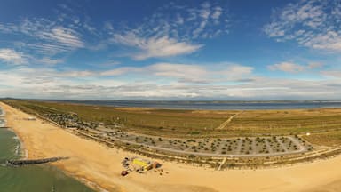 Un paisaje costero con playa, un estacionamiento y una carretera que lleva a una costa distante.