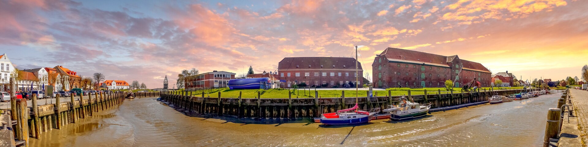 A canal with boats, a large building, and a sunset sky.