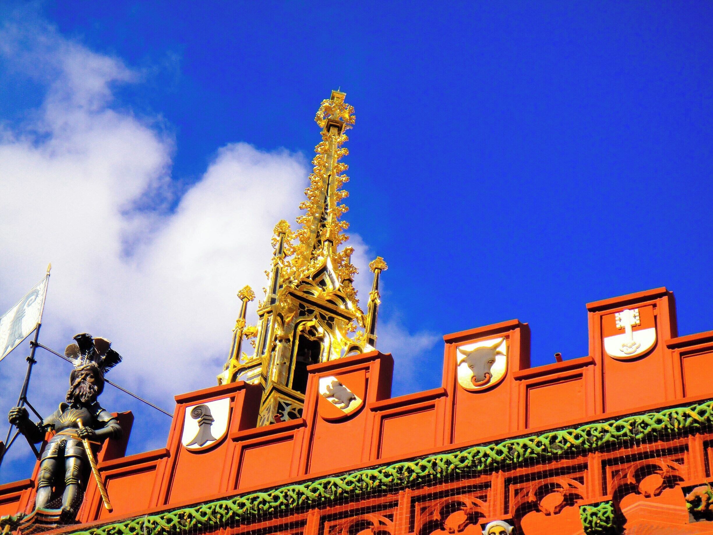 A golden spire atop a red building with a statue of a figure holding a flag.