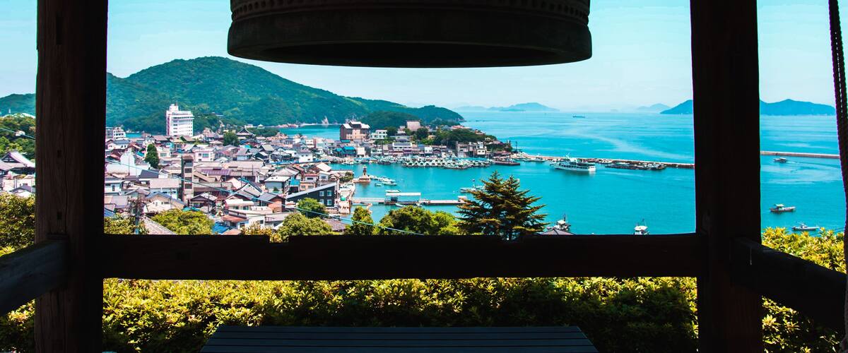 A coastal town with a prominent bell tower, lush greenery, and a clear view of the sea.