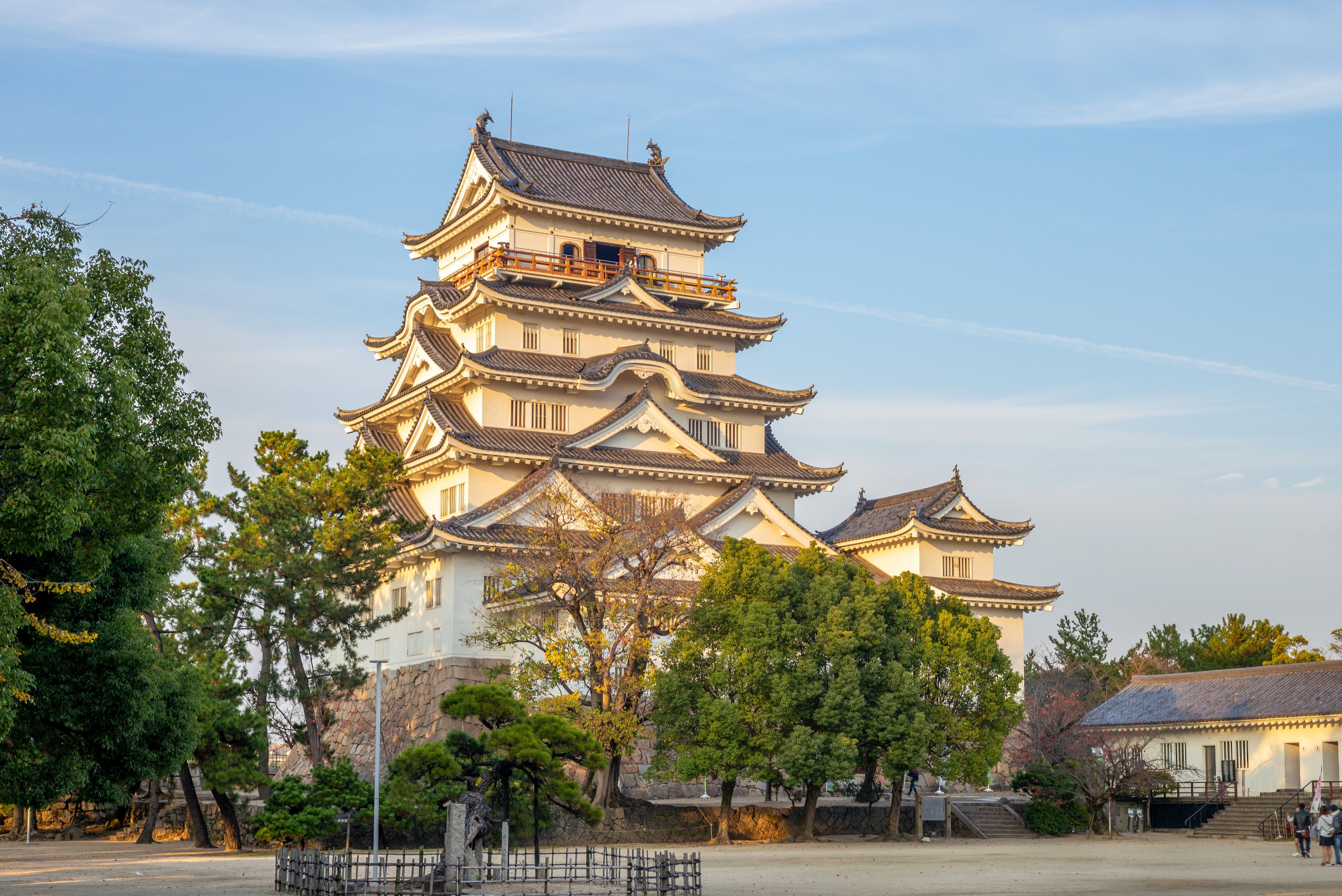 A traditional multi-tiered pagoda with ornate roof tiles, surrounded by trees and a stone wall.