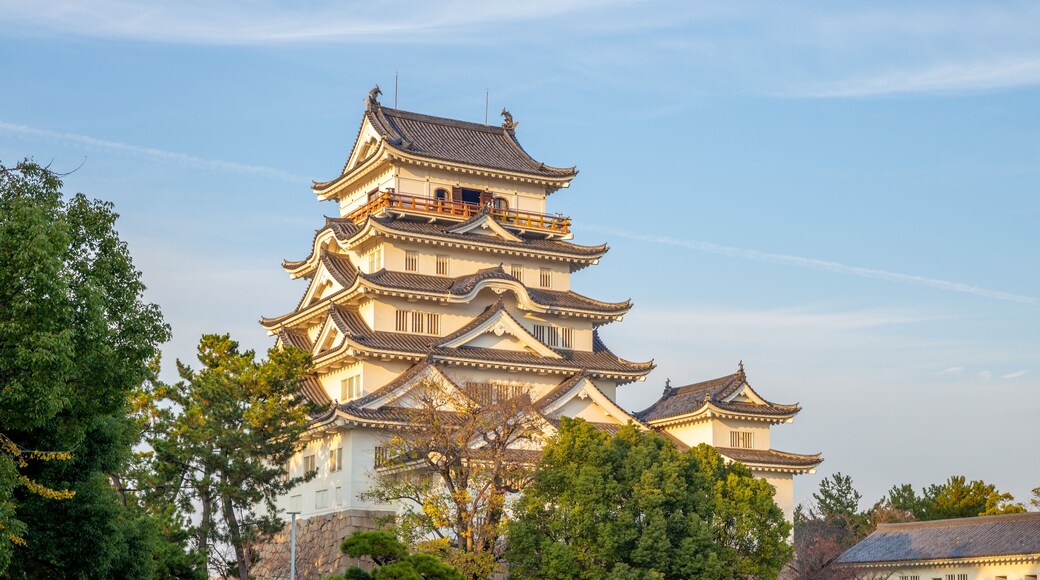 A traditional multi-tiered pagoda with ornate roof tiles, surrounded by trees and a stone wall.