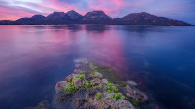 A mountain range reflected in calm waters with a vibrant sky.