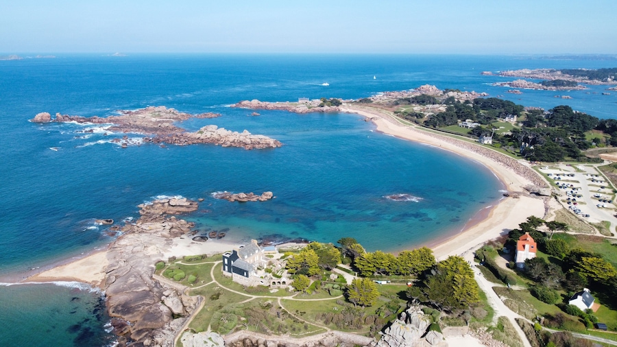 Un paysage côtier caractérisé par une plage en forme de courbe, des affleurements rocheux et un vaste ensemble de bâtiments.