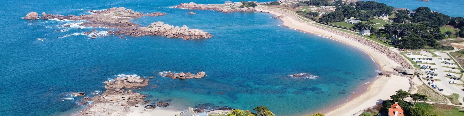 Un paysage côtier caractérisé par une plage en forme de courbe, des affleurements rocheux et un vaste ensemble de bâtiments.