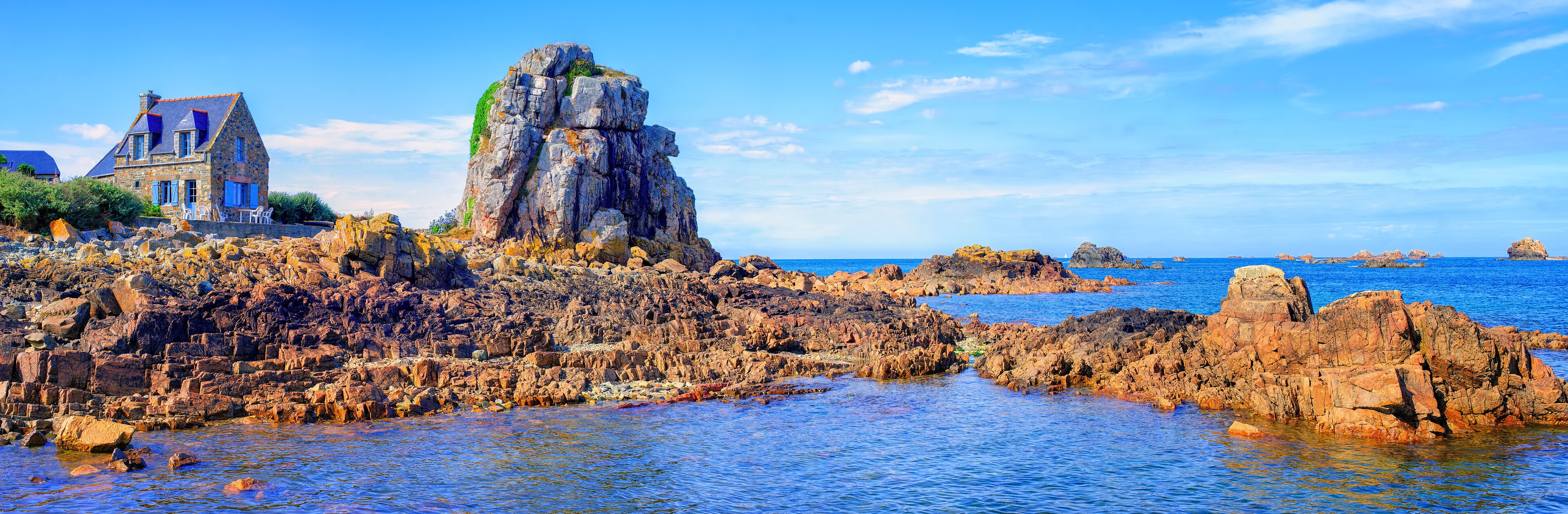 A coastal landscape with a prominent rocky outcrop and a stone building with blue shutters.