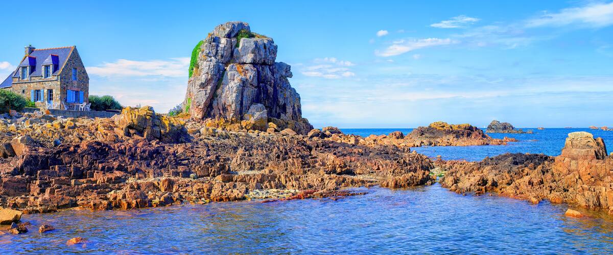 A coastal landscape with a prominent rocky outcrop and a stone building with blue shutters.