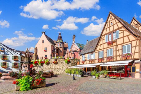 Ein Kopfsteinpflasterplatz mit traditionellen Fachwerkhäusern, einer Kirche mit einem Kirchturm und Blumenkästen an den Gebäuden.