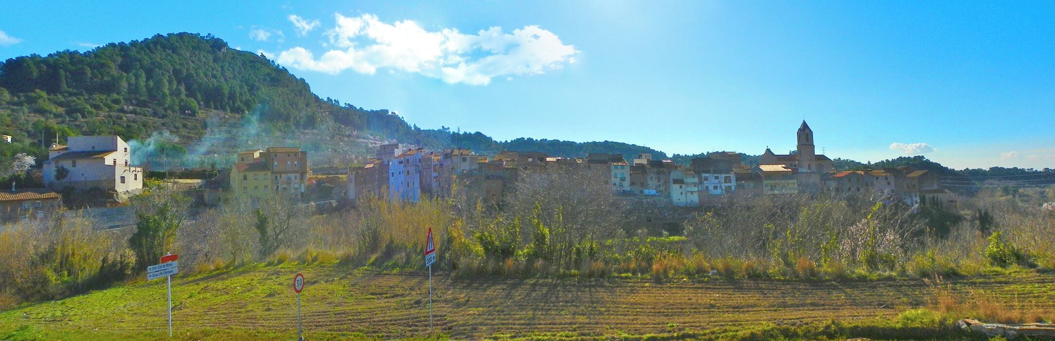 A rural landscape with terraced fields, a village with colorful buildings, and a hill with a church tower.
