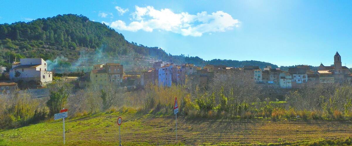 A rural landscape with terraced fields, a village with colorful buildings, and a hill with a church tower.