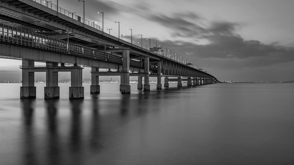 A long bridge with multiple lanes and streetlights, spanning over a body of water.