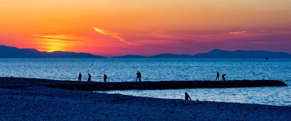 A beach at sunset with silhouettes of people and a pier extending into the water.