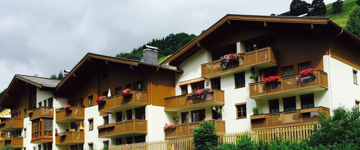 A row of chalet-style buildings with wooden balconies and flower boxes, situated beside a flowing river.