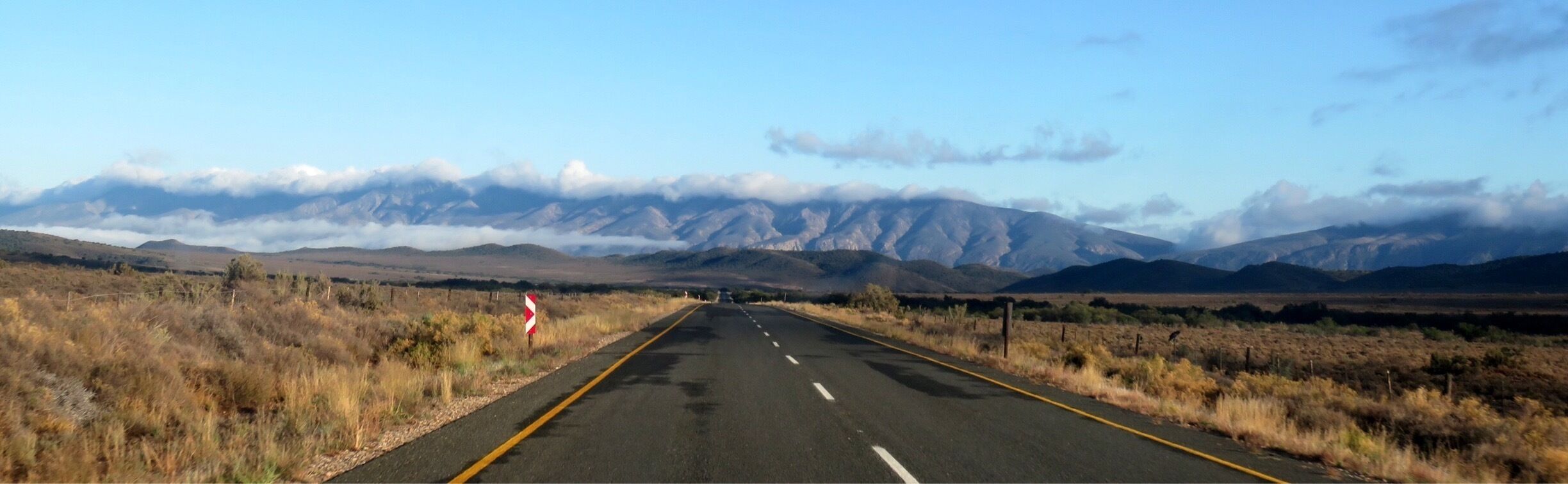 A straight road with mountains in the distance and a clear sky.