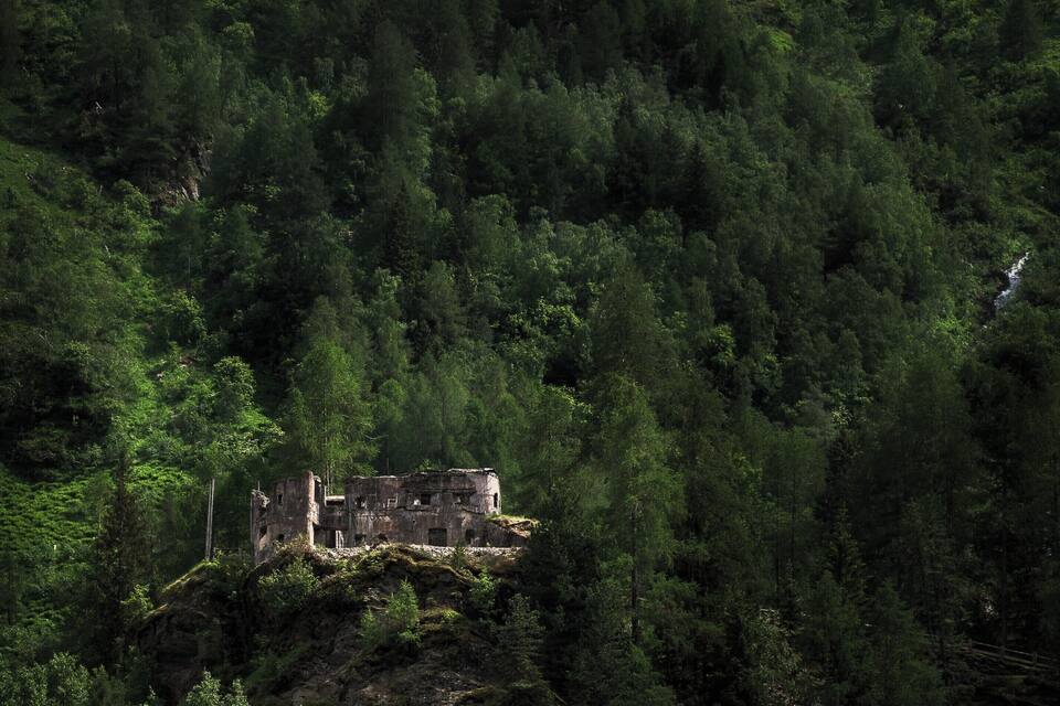 Una montagna ricoperta di boschi con un castello in rovina e cascate a gradoni.