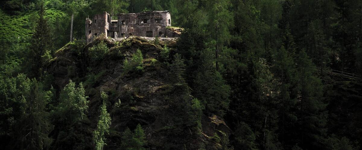 A forested mountain with a ruined castle and cascading waterfalls.