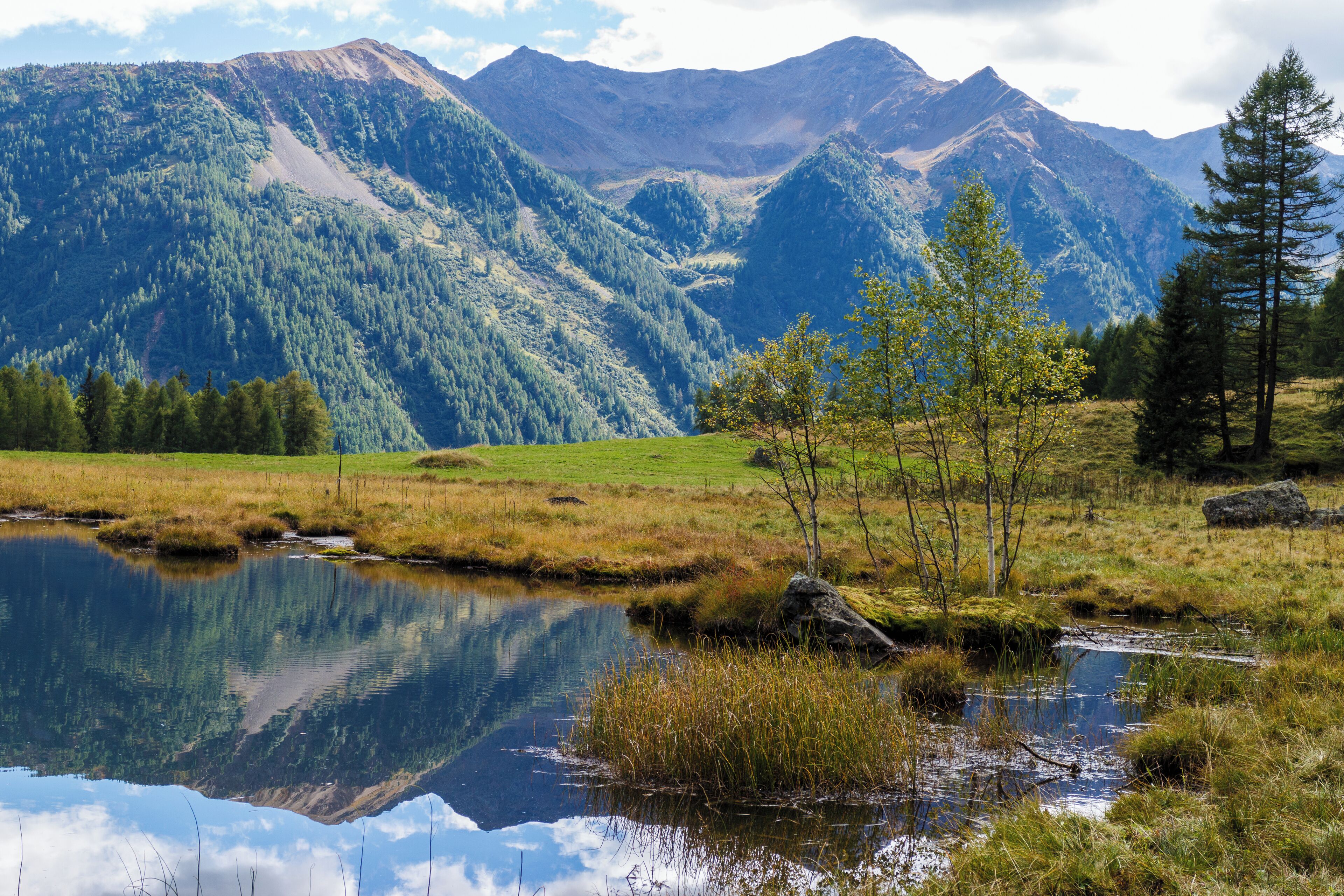 Paisaje montañoso con un lago que refleja árboles y montañas.