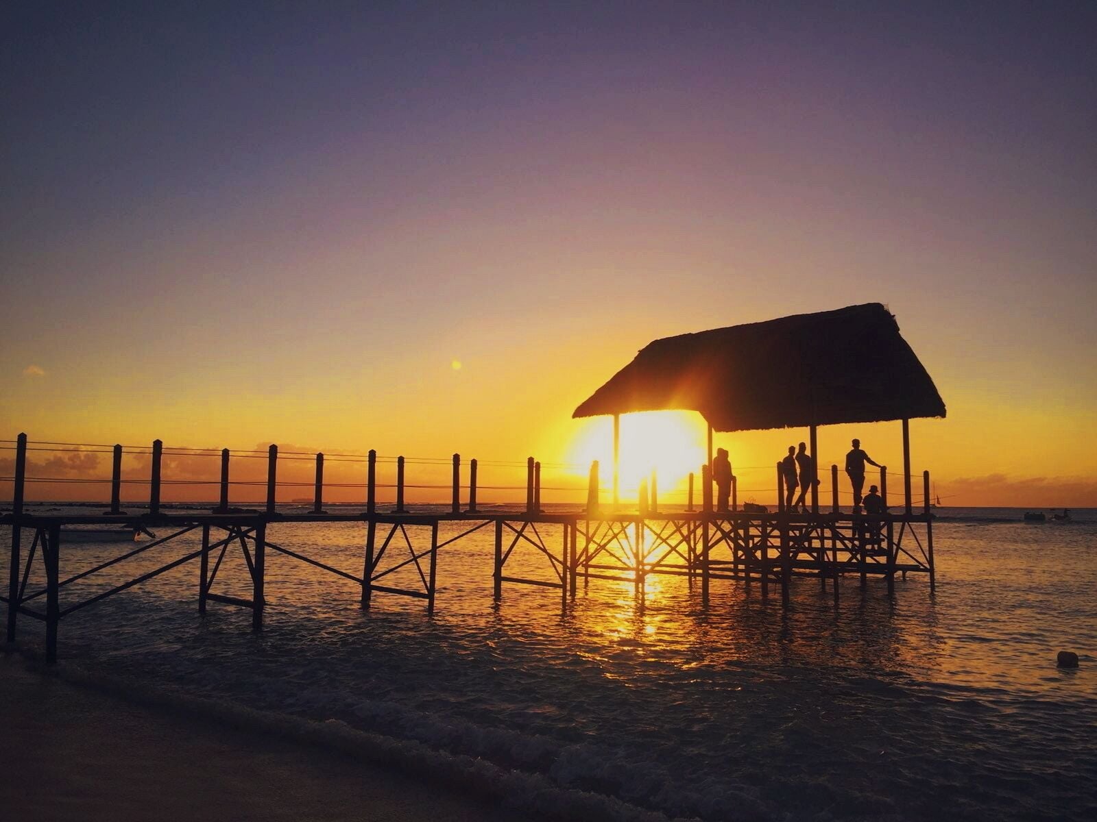A pier at sunset with people standing under a shelter.