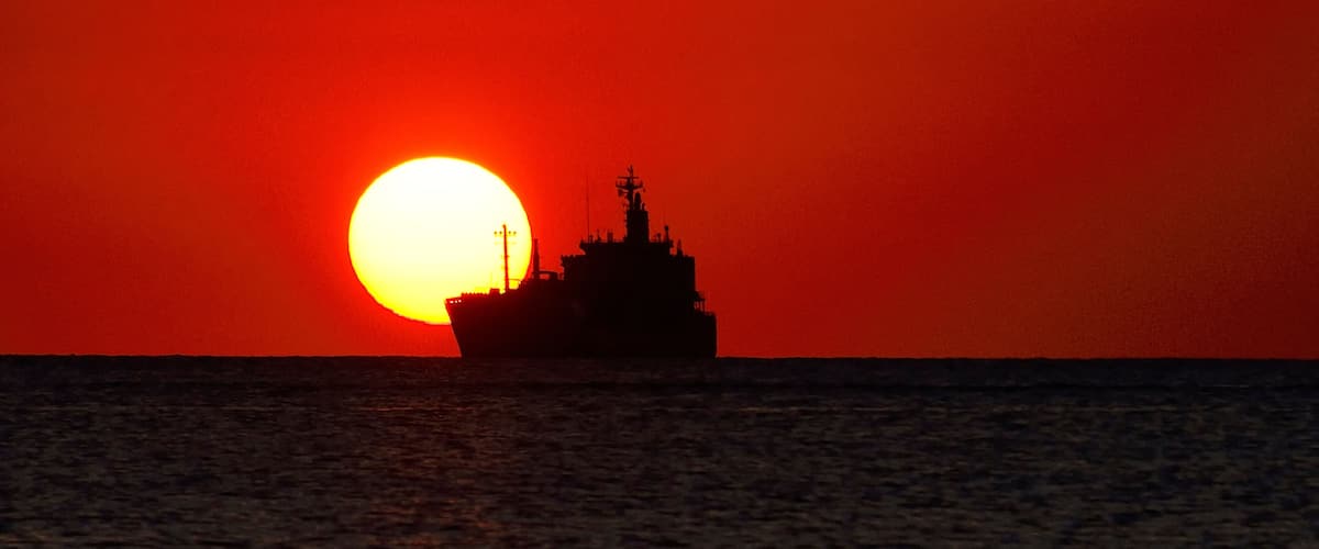 A ship silhouetted against a sunset with a vibrant red sky.