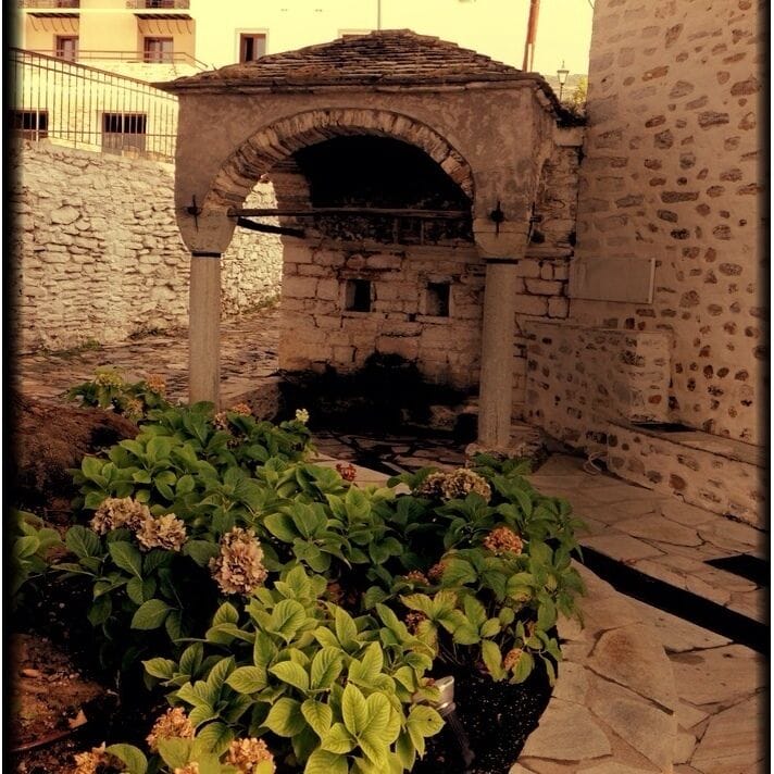 A stone archway, a stone wall, and a garden with hydrangea plants.