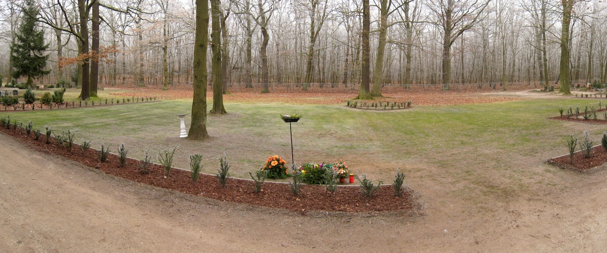 A cemetery with neatly trimmed grass, trees, and flower beds.