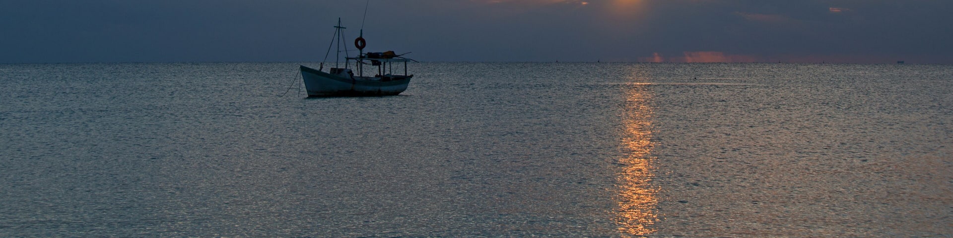 A boat on calm water with a sunset in the background.