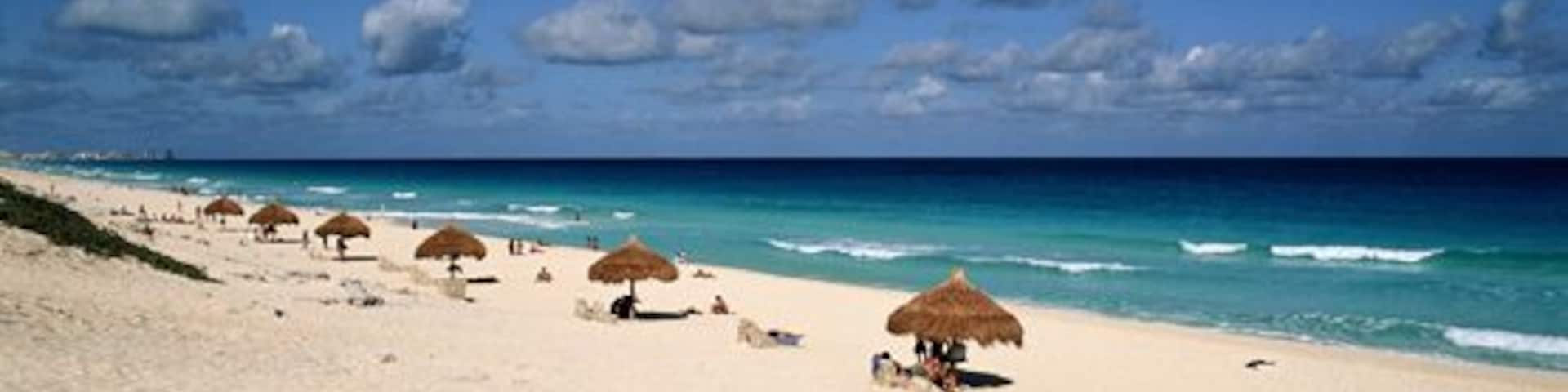 Una playa con sombrillas de paja y aguas turquesas tranquilas.